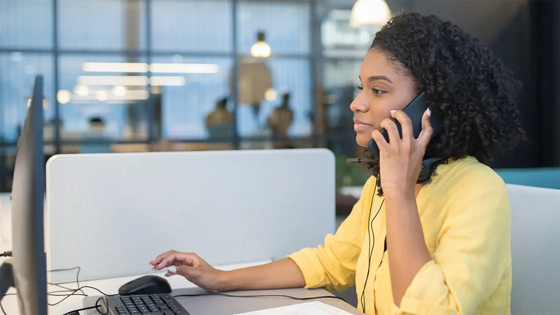 persona haciendo una llamada en su teléfono en frente de una computadora